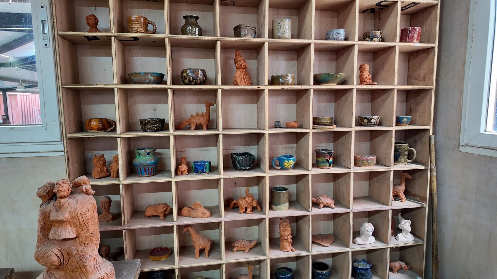 Shelves of glazed pots, mugs and terracotta figures made by students.