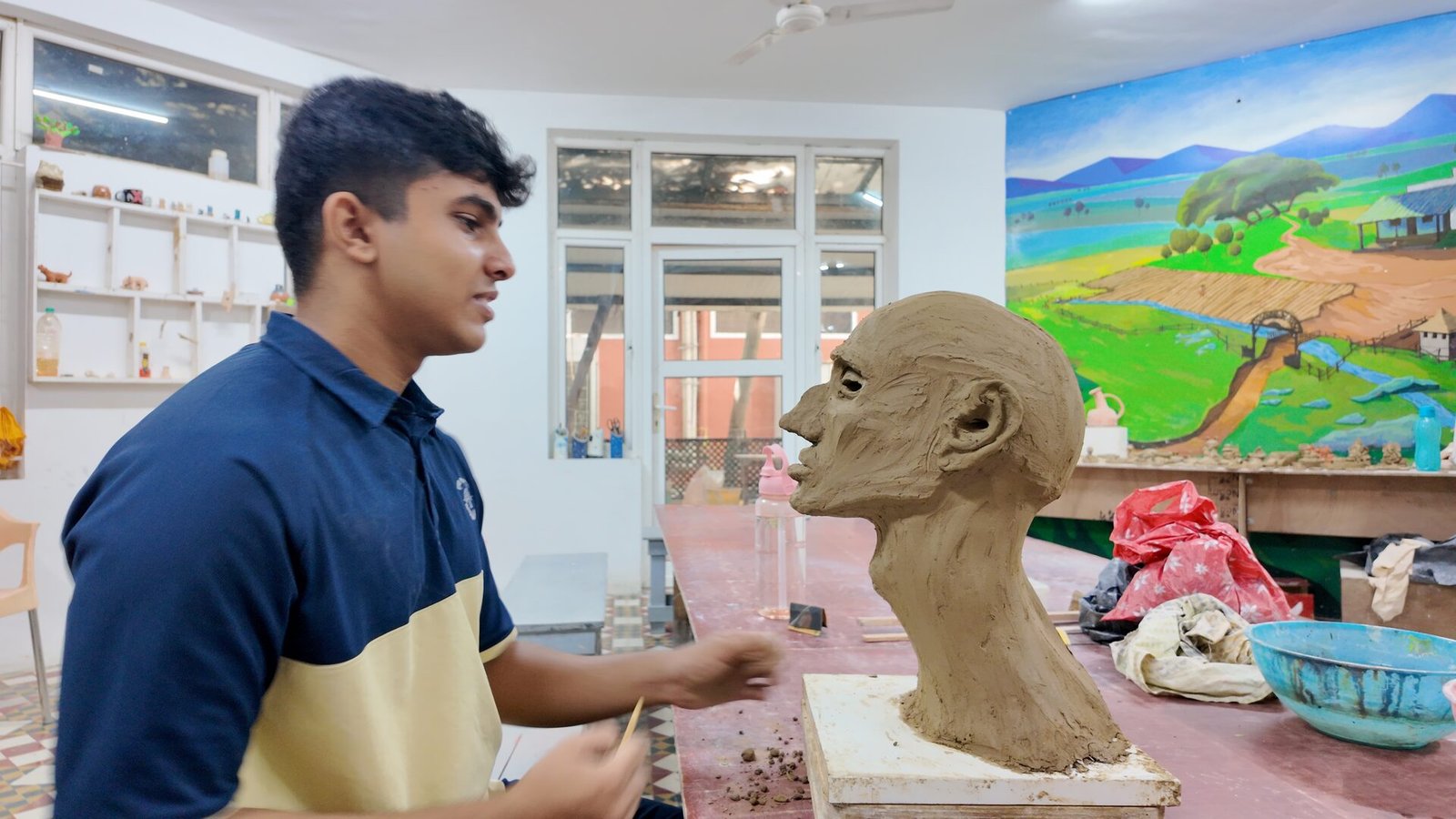 A student sculpting a clay head in the art studio.