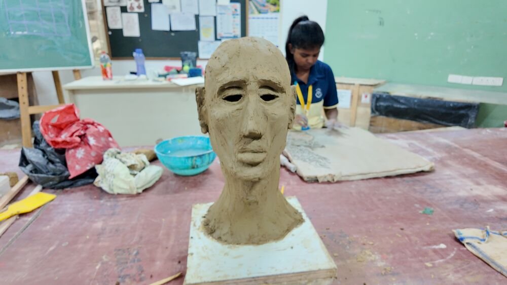 A student beside the clay head she is sculpting.