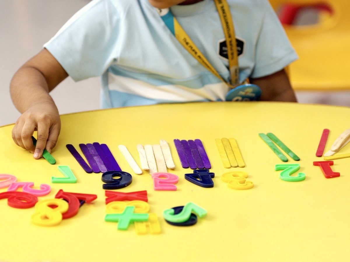 Hands arranging coloured number tiles and counting sticks.