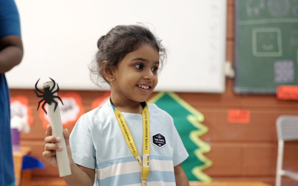 A young girl smiling as she shows a spider puppet.