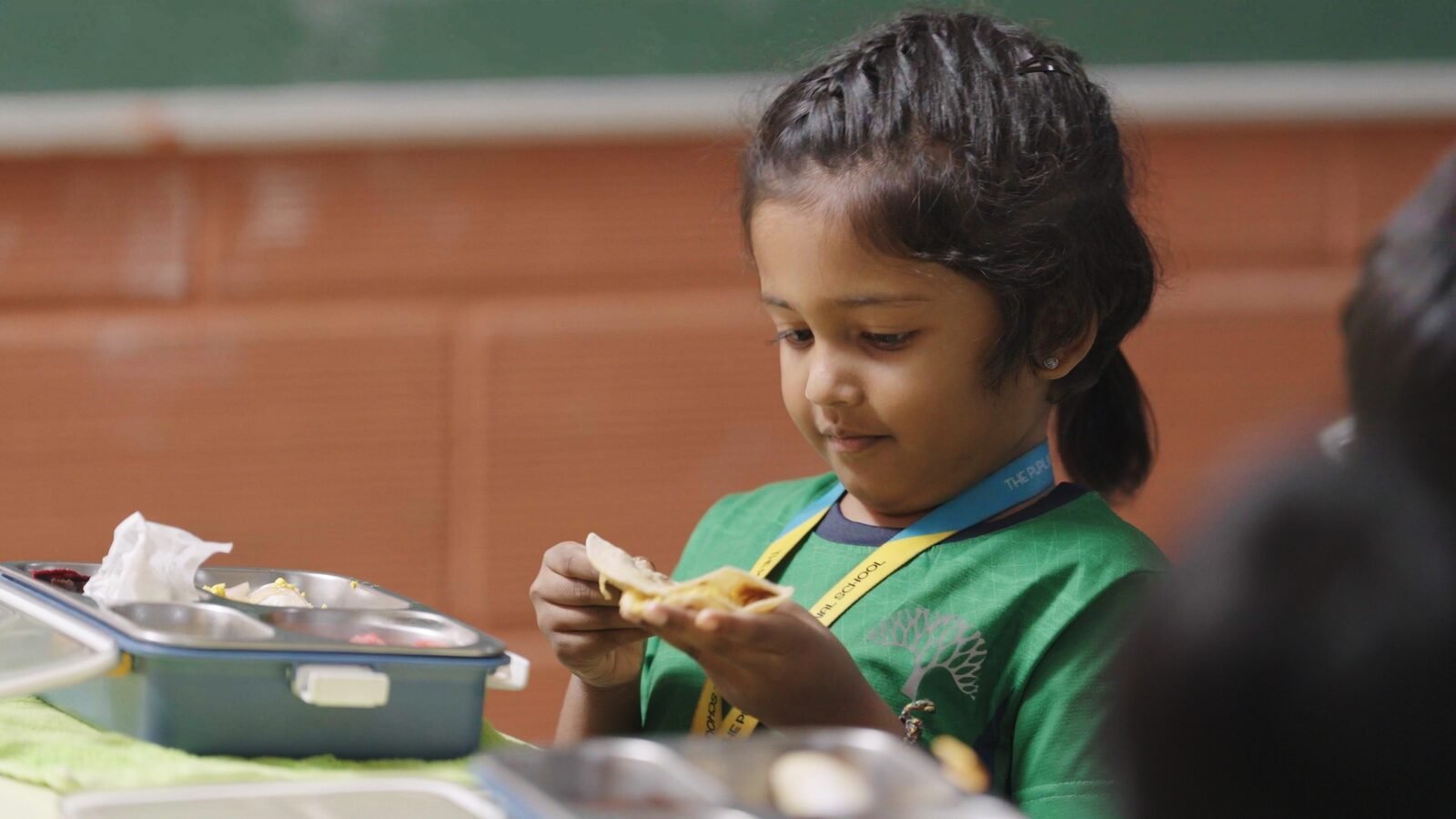 A young student looking at the wrap from her bento box lunch.