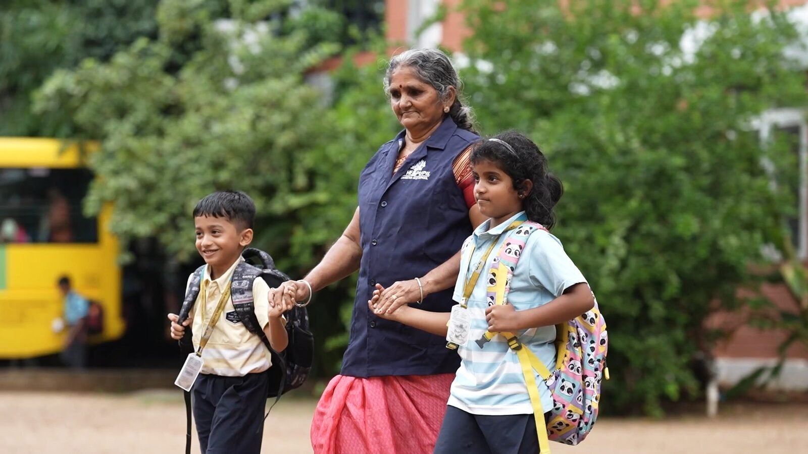 A bus attendant holding hands with two students on their way in from the bus.