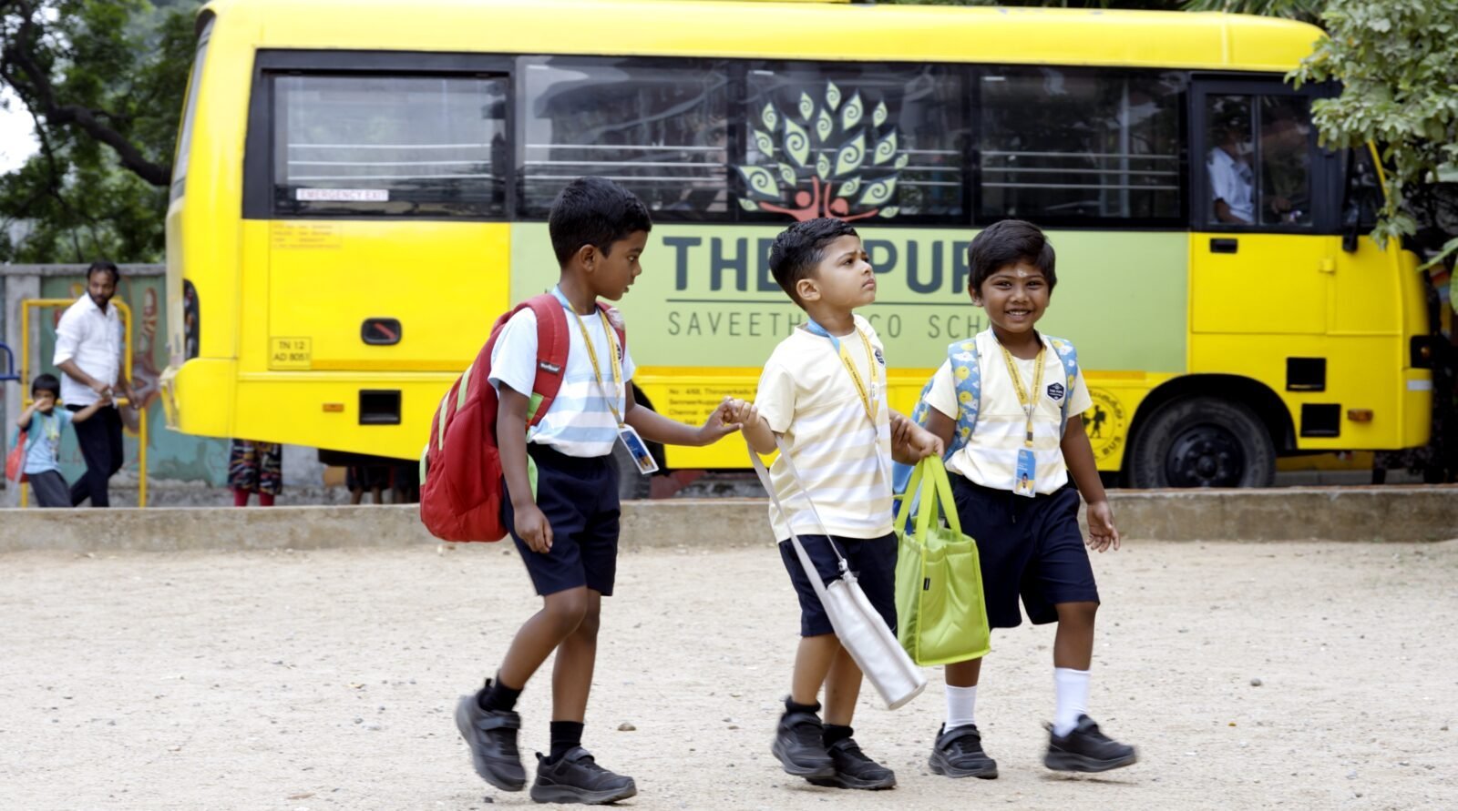 Three young students walking together past a school bus.