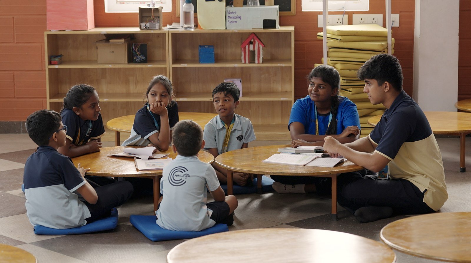Senior students working with younger children around a low round table.
