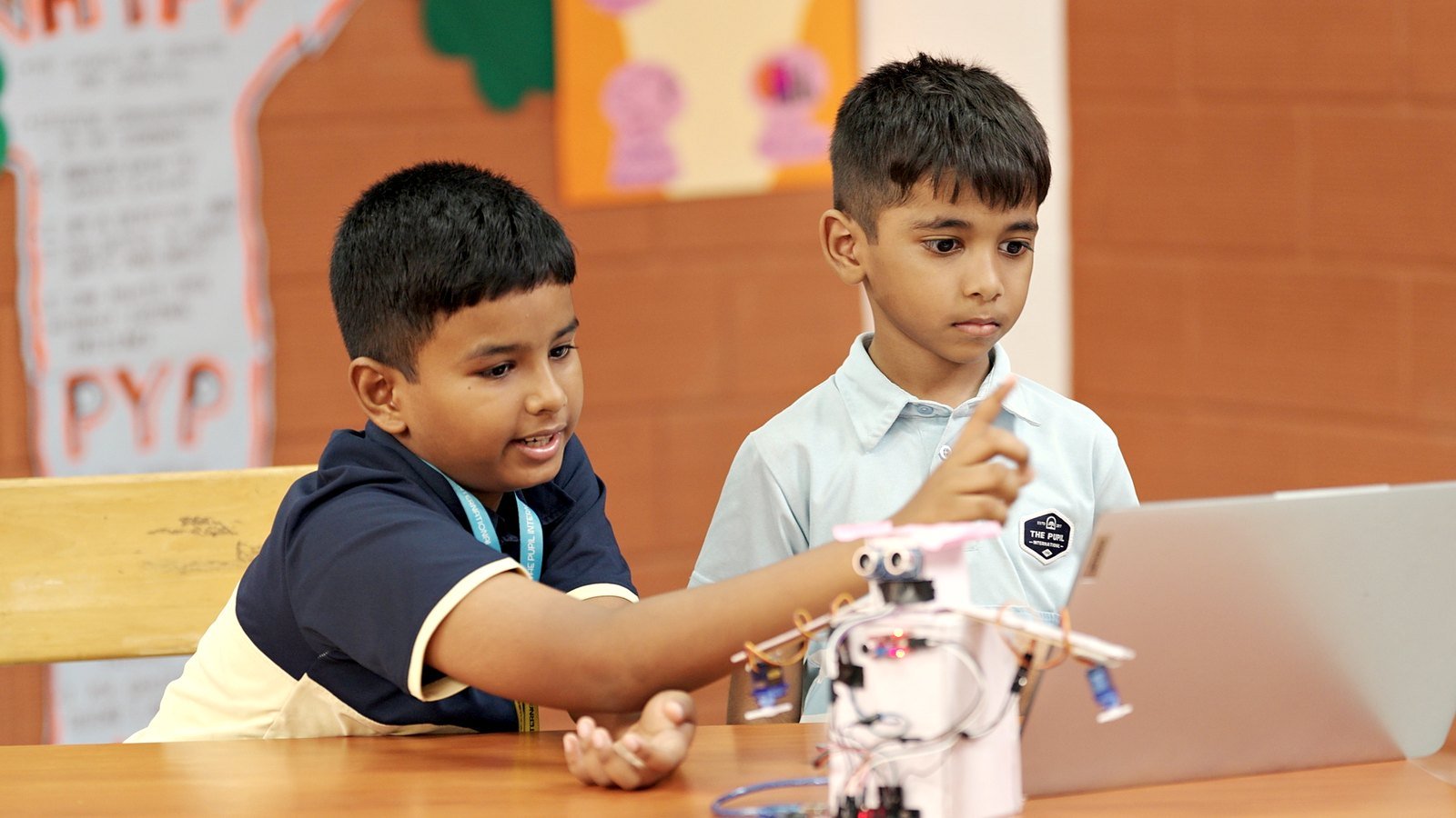 A boy laughing beside his paper rocket, with a friend next to him.