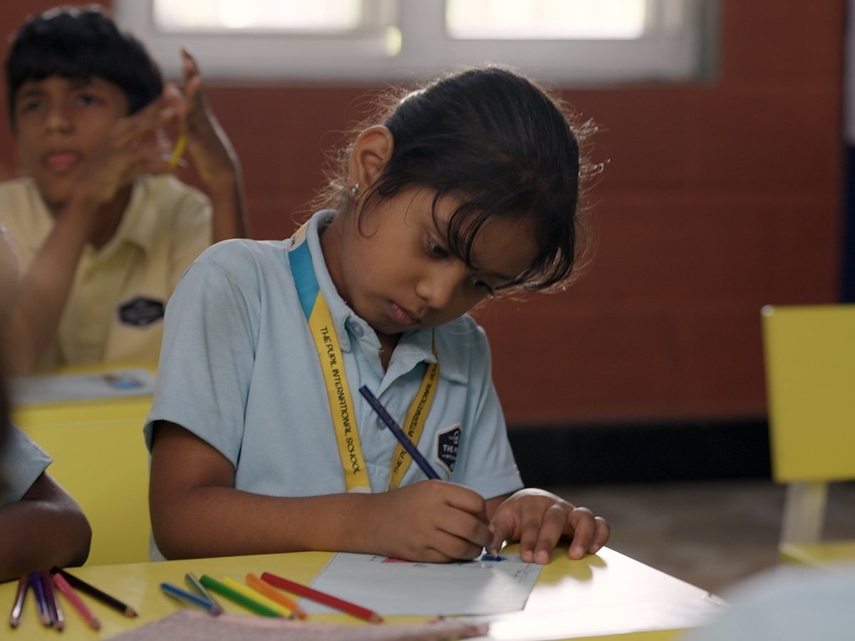 A girl drawing at her desk, with coloured pencils beside her.
