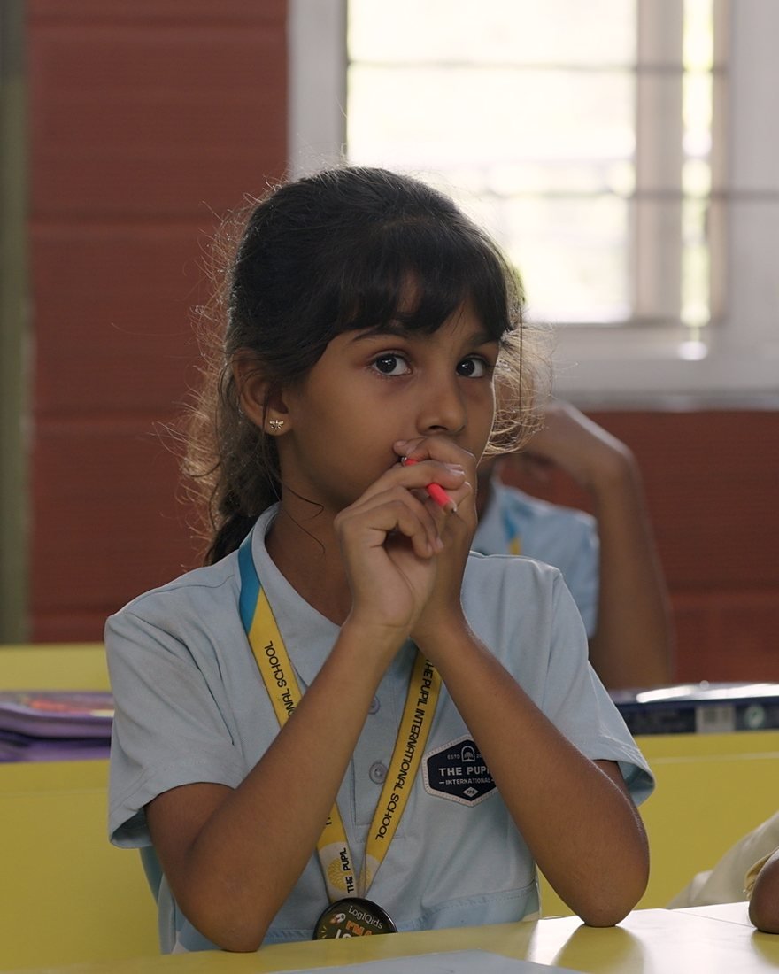 A girl thinking about a question at her desk.