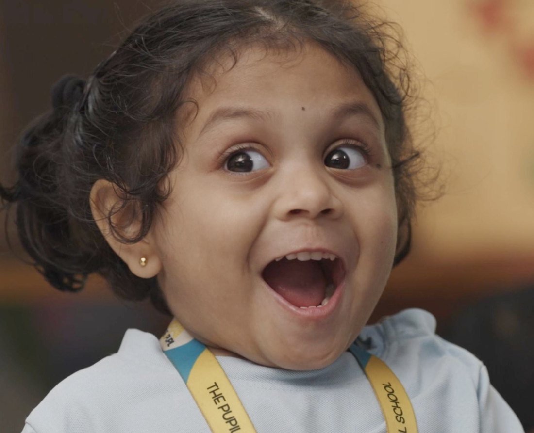 A young girl laughing with her arms out in class.