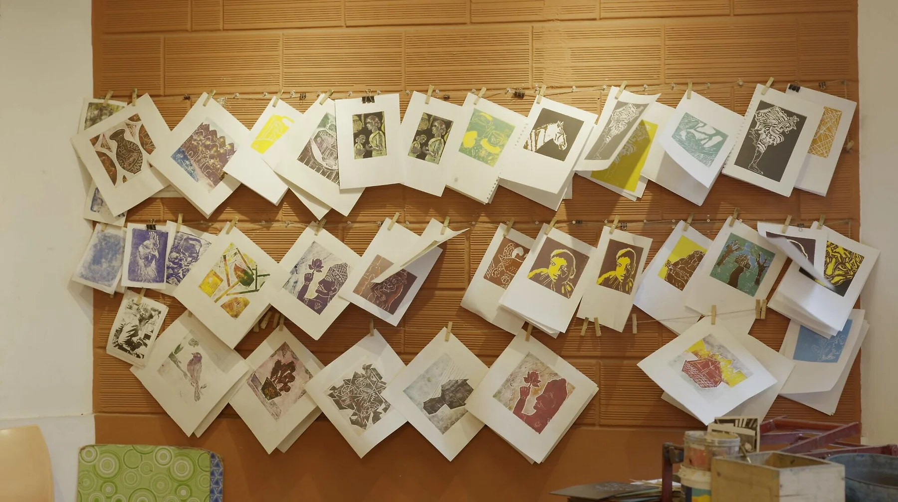 Rows of student lino prints pegged up to dry on the studio wall.