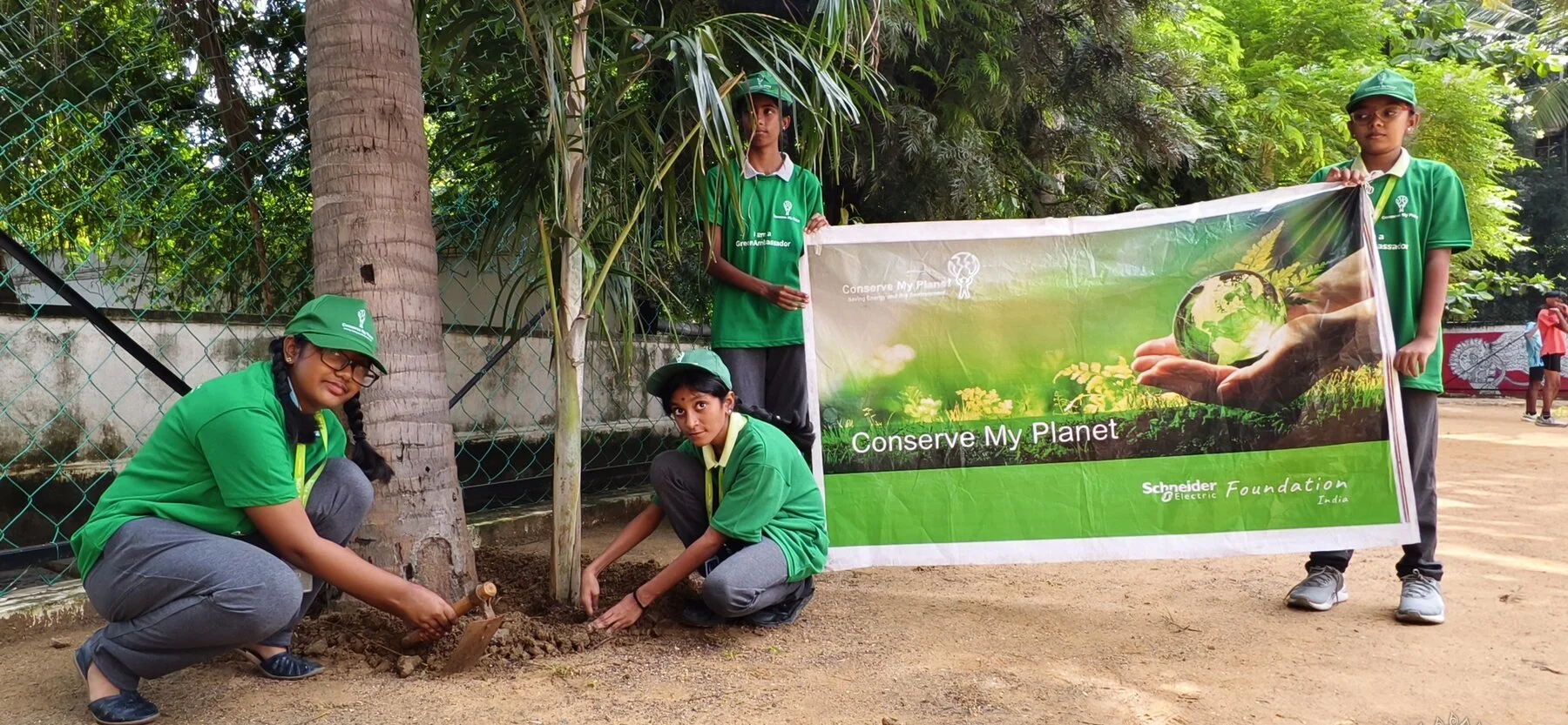 Eco Warriors students planting a sapling beside a Conserve My Planet banner.