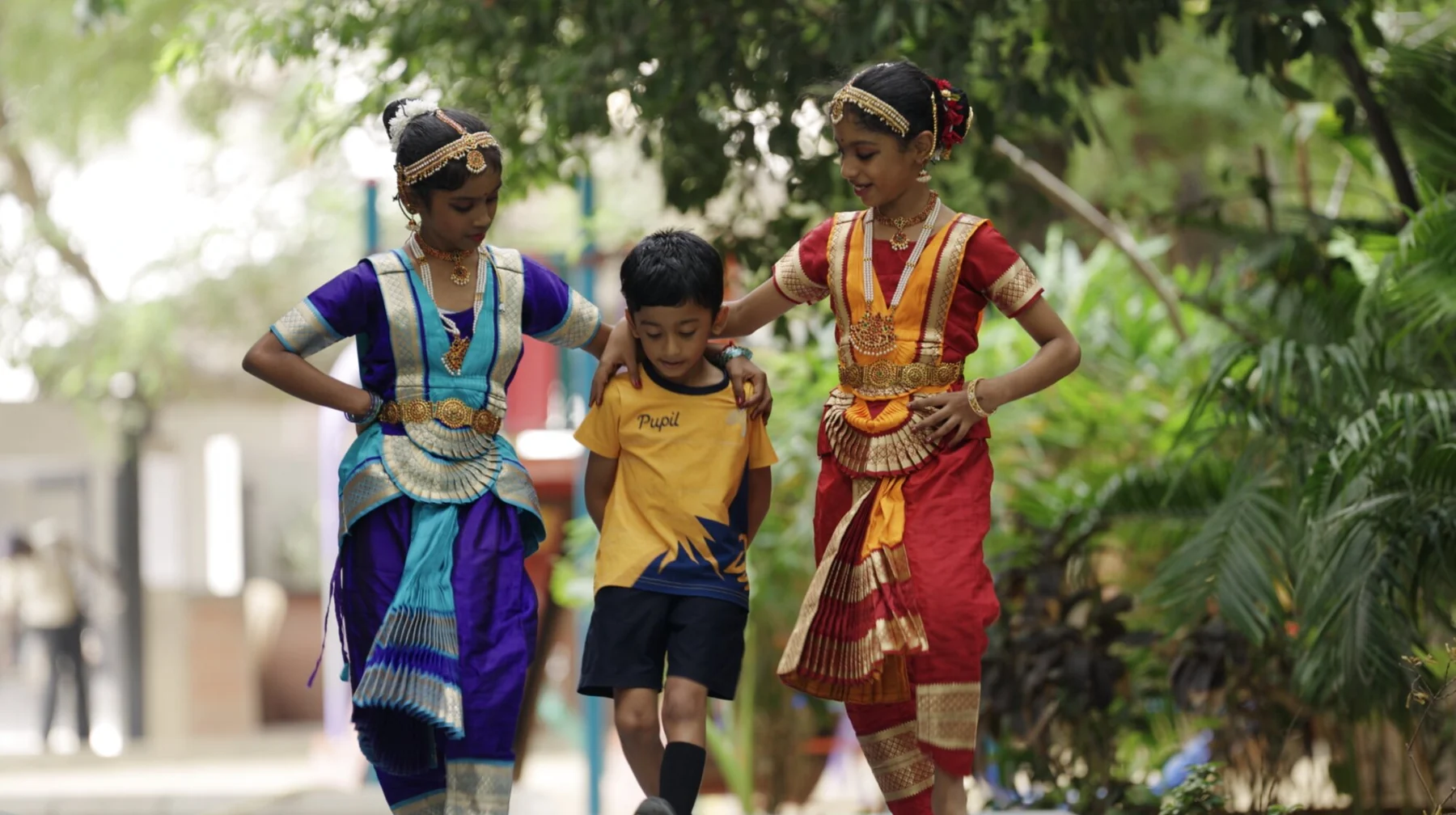 Two Bharatanatyam dancers in costume walking with a younger student.