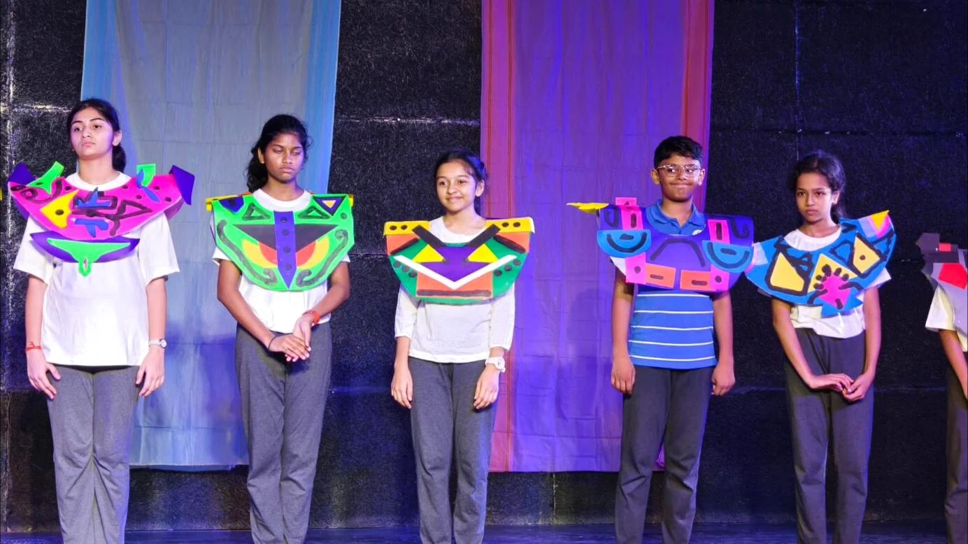 Theatre Club students on stage in colourful handmade costumes.
