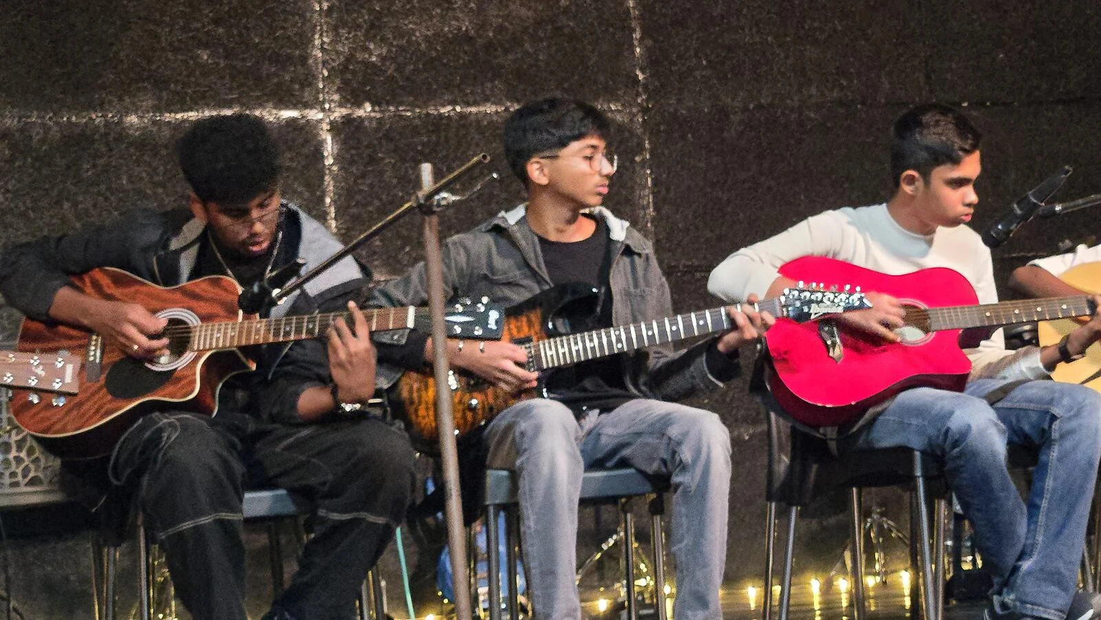 Three students playing guitar together on stage.