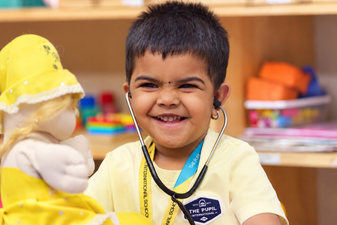 Smiling child using a stethoscope during pretend play with a doll at The Pupil International School, Chennai.