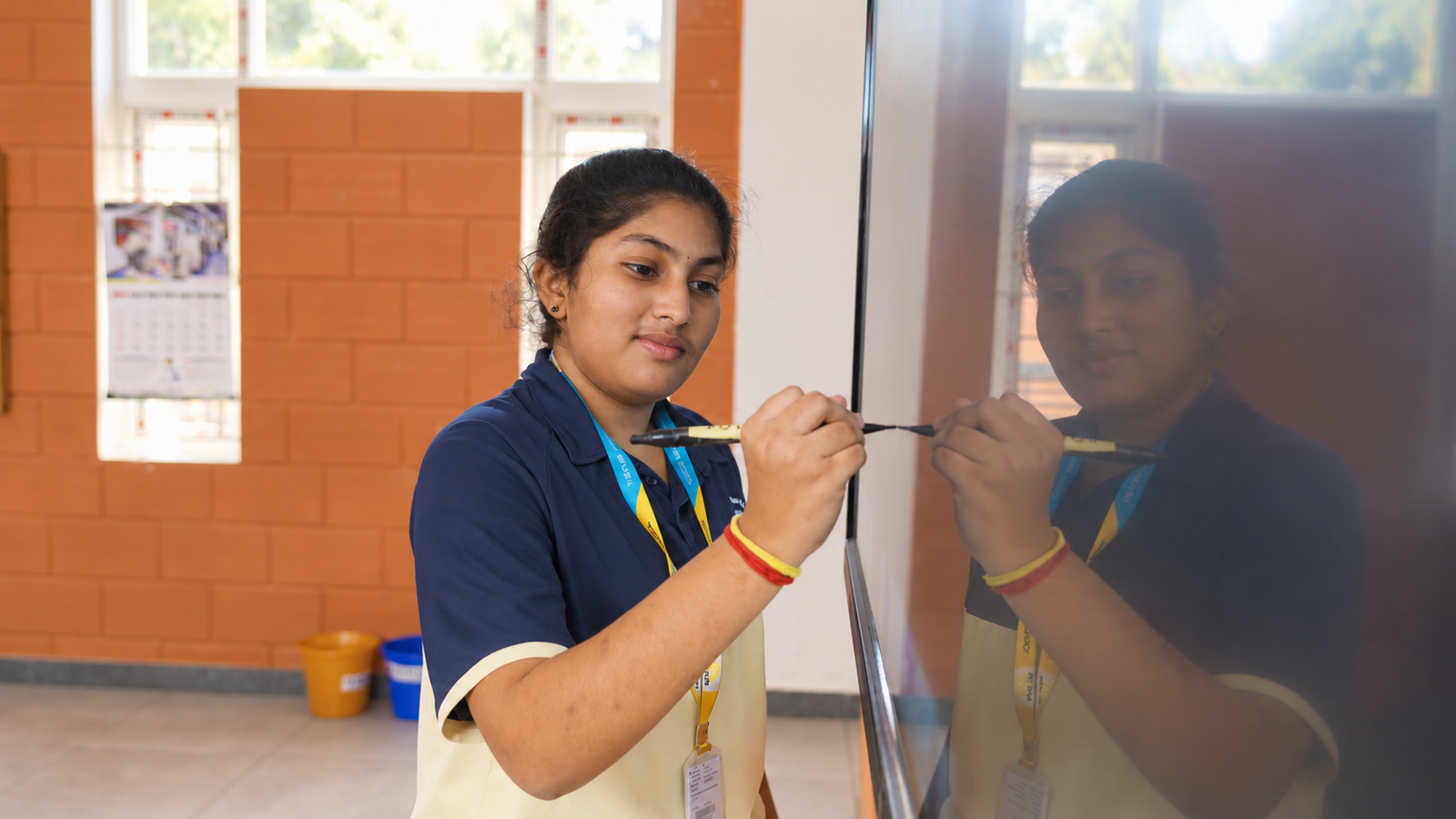 Student writing on a reflective classroom board at The Pupil International School, Chennai.