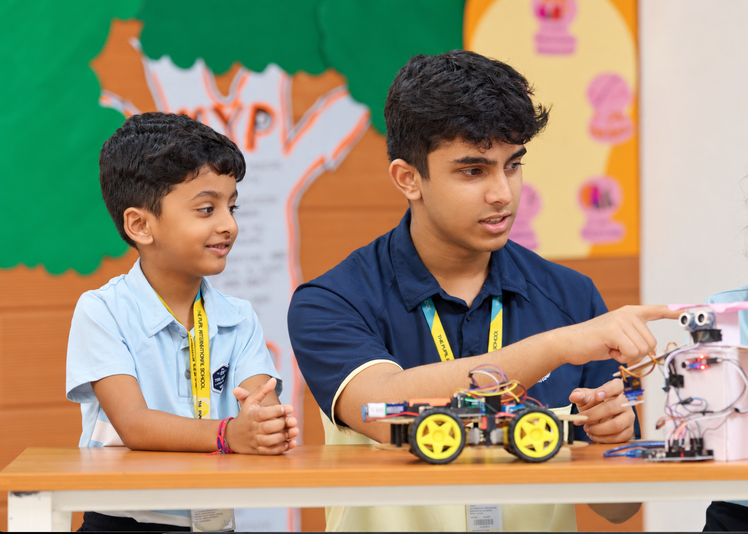 Older student demonstrating handmade robots to a younger pupil at The Pupil International School.